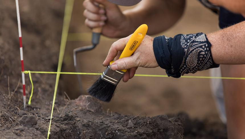 Archaeologists using brushes on a dig to find artifacts